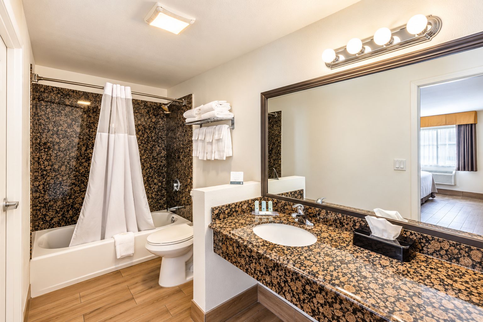Een moderne badkamer met bad, toilet en wastafel, met een grote spiegel en douchegordijn.
