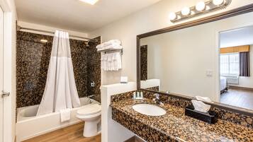 Een moderne badkamer met bad, toilet en wastafel, met een grote spiegel en douchegordijn.