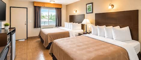 Habitación de hotel con dos camas, un escritorio con computadora, una ventana con cortinas y una lámpara de pared.