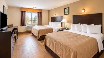 A hotel room with two beds, a desk, a TV, and a window with curtains.