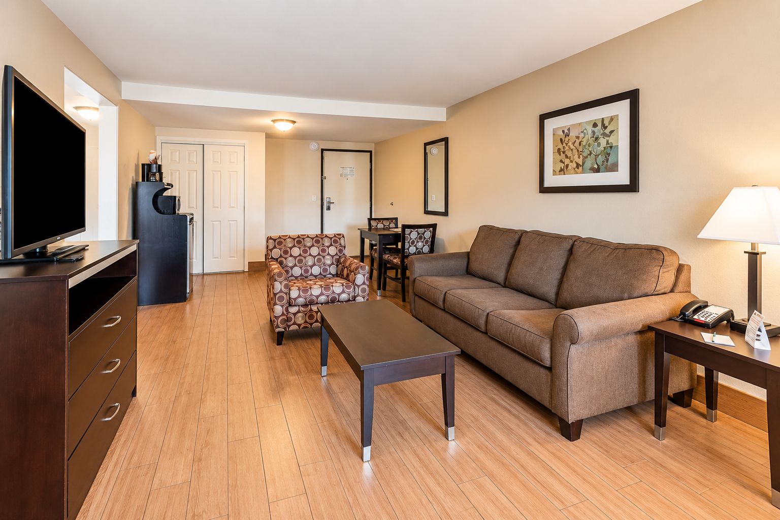 A modern living room with a sofa, armchair, coffee table, TV, and a desk with a lamp.