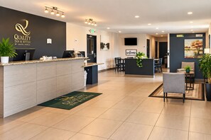 A hotel reception area with a reception desk, a 'Welcome' sign, a television, and a seating area with chairs and a table. - Quality Inn & Suites near Downtown Bakersfield (Bakersfield)