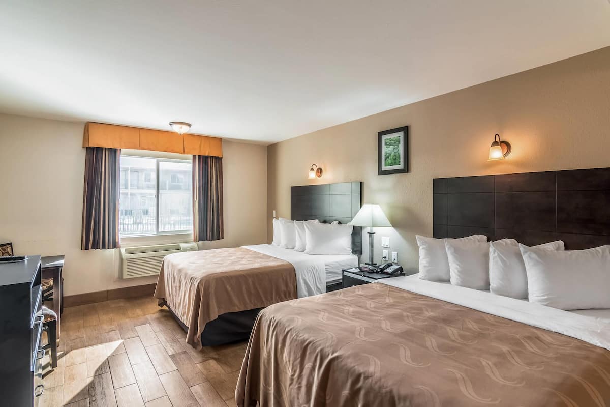A hotel room with two beds, a desk, a lamp, and a window with curtains.