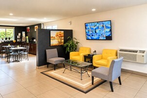 Un hall d’hôtel moderne comprenant un espace repas, des sièges disposés autour d’une table basse en verre et un grand téléviseur à écran plat fixé au mur.