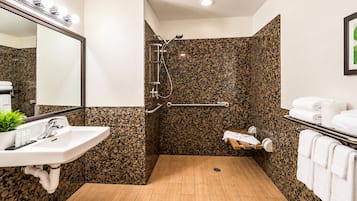 A bathroom with a sink, mirror, shower, and towel rack.