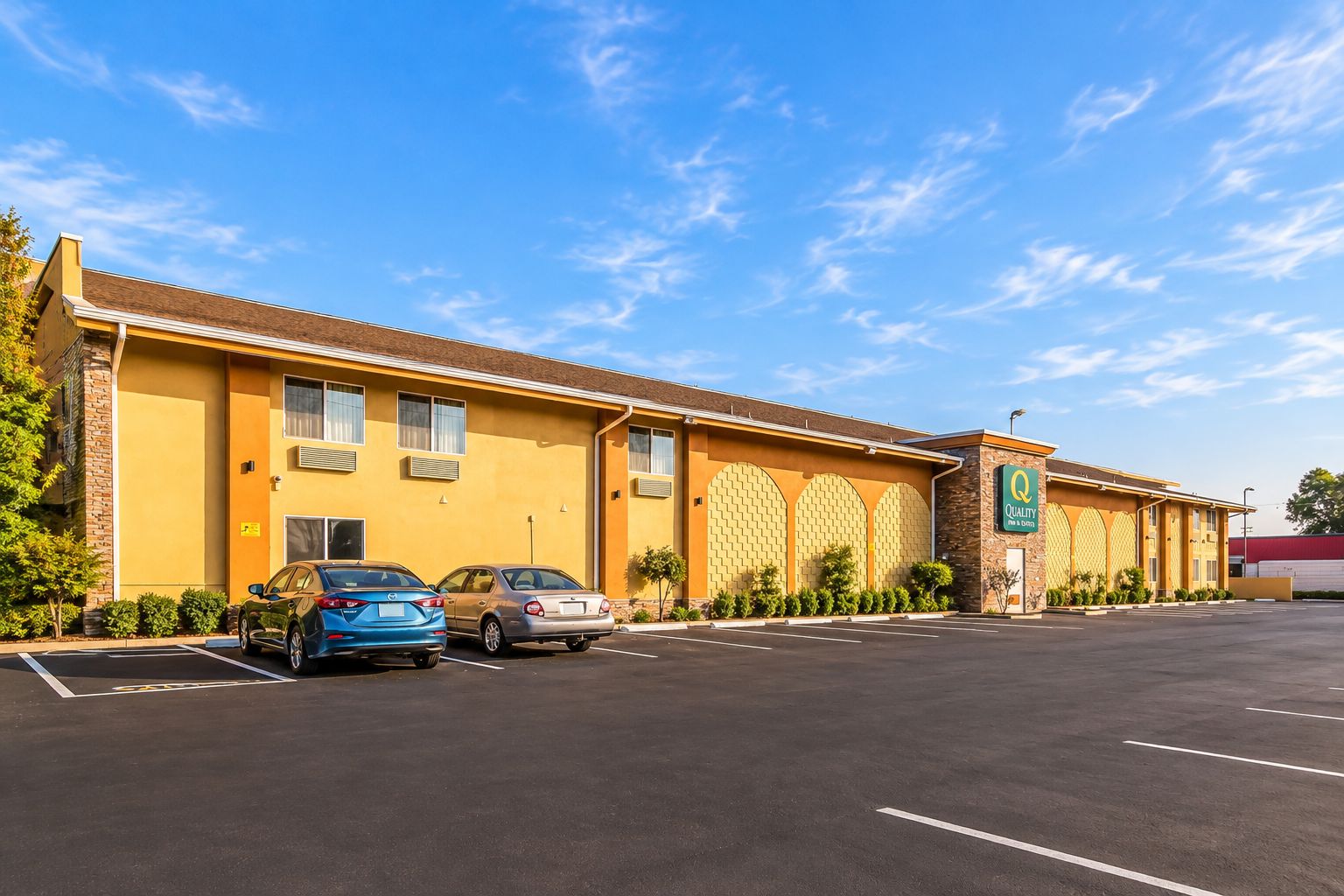 A hotel with a parking lot, two cars parked in front, and a clear blue sky.