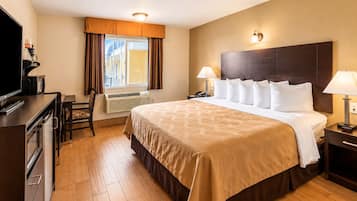 Una habitación de hotel con una cama grande, lámparas de noche, un escritorio con televisor y una ventana con cortinas.