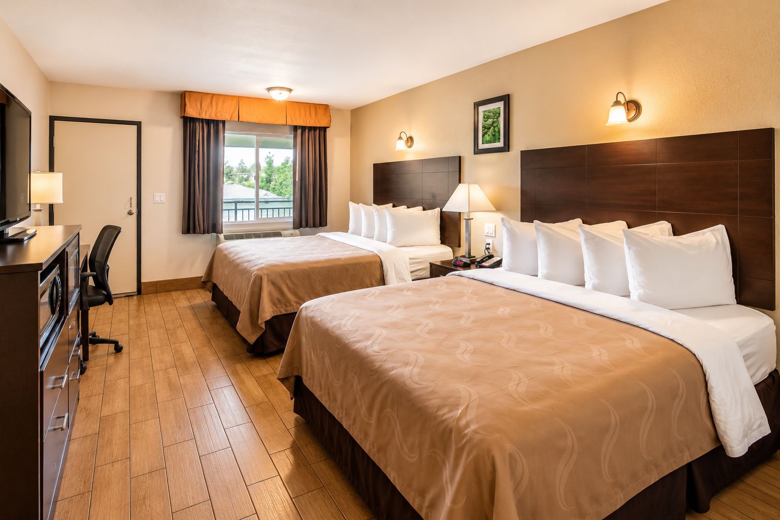 Une chambre d’hôtel avec deux lits, un bureau, une chaise, une télévision et une fenêtre avec des rideaux.