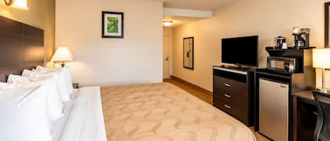 A hotel room with a bed, a desk with a computer, a television, and a coffee maker.