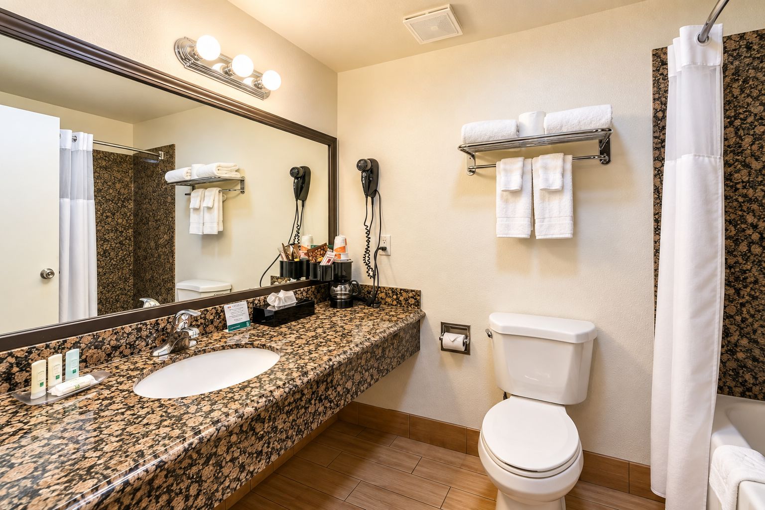 Un baño con lavamanos de encimera de granito, inodoro, cortina de ducha y toallero.