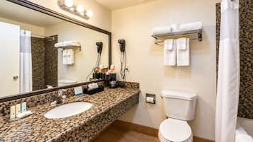 Un baño con lavamanos de encimera de granito, inodoro, cortina de ducha y toallero.