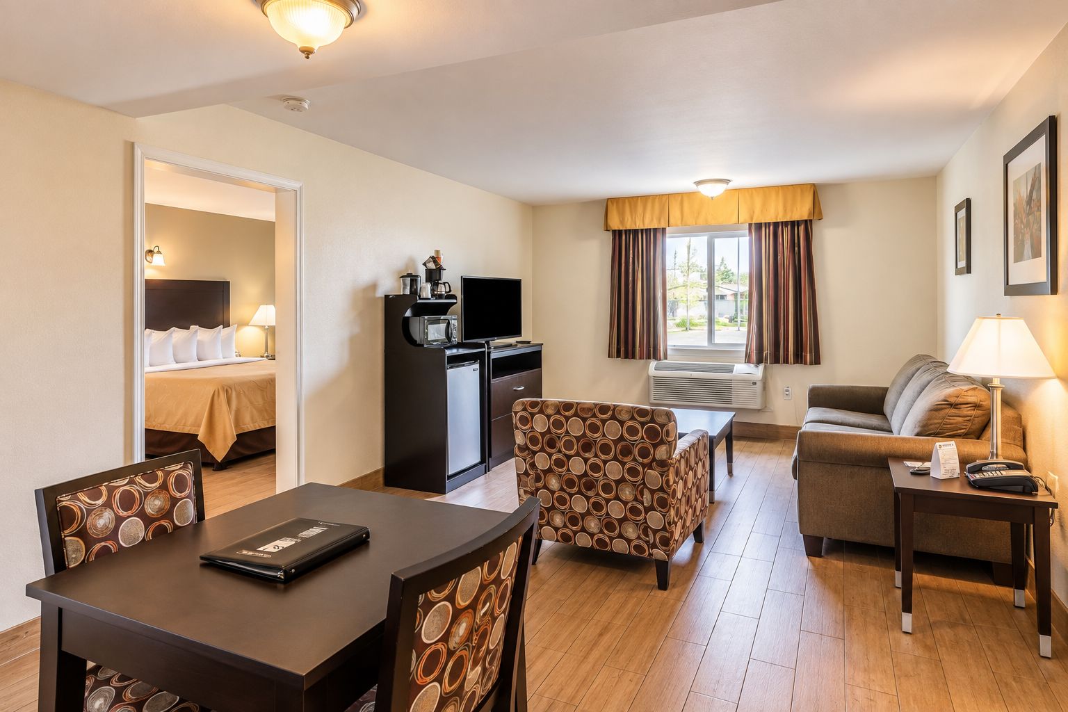 Una habitación de hotel con cama, escritorio con computadora, mesa de comedor con sillas, sofá y una pequeña mesa con lámpara.