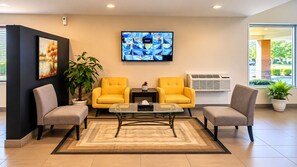 A lobby with two yellow armchairs, a glass coffee table, a painting, a television, and a potted plant. - Quality Inn & Suites near Downtown Bakersfield (Bakersfield)