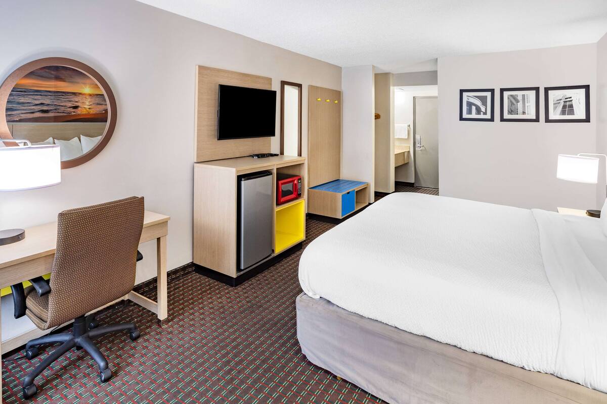 A hotel room with a bed, desk, chair, television, microwave, and a small refrigerator.