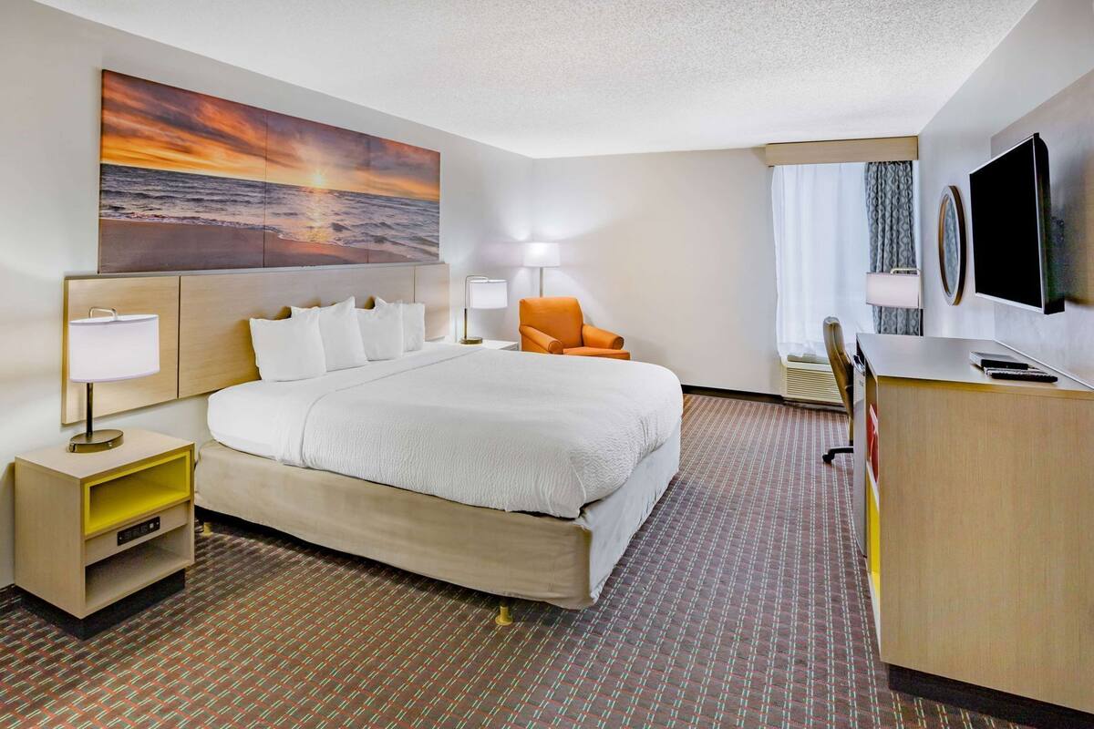 A hotel room with a bed, a desk, a TV, a painting, and a lamp.