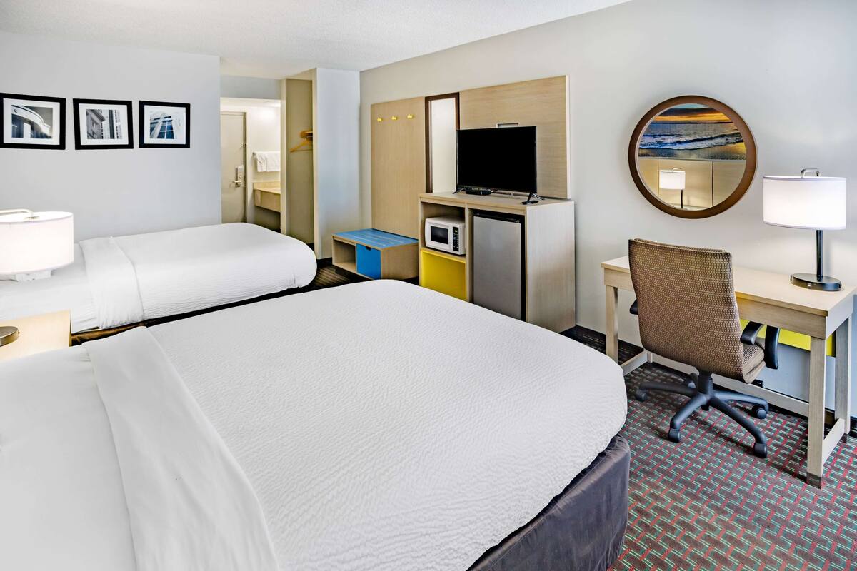 A hotel room with two beds, a desk with a computer, a TV, a microwave, and a small seating area.