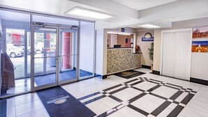 A hotel lobby with a reception desk, a check-in counter, and a large glass door entrance.