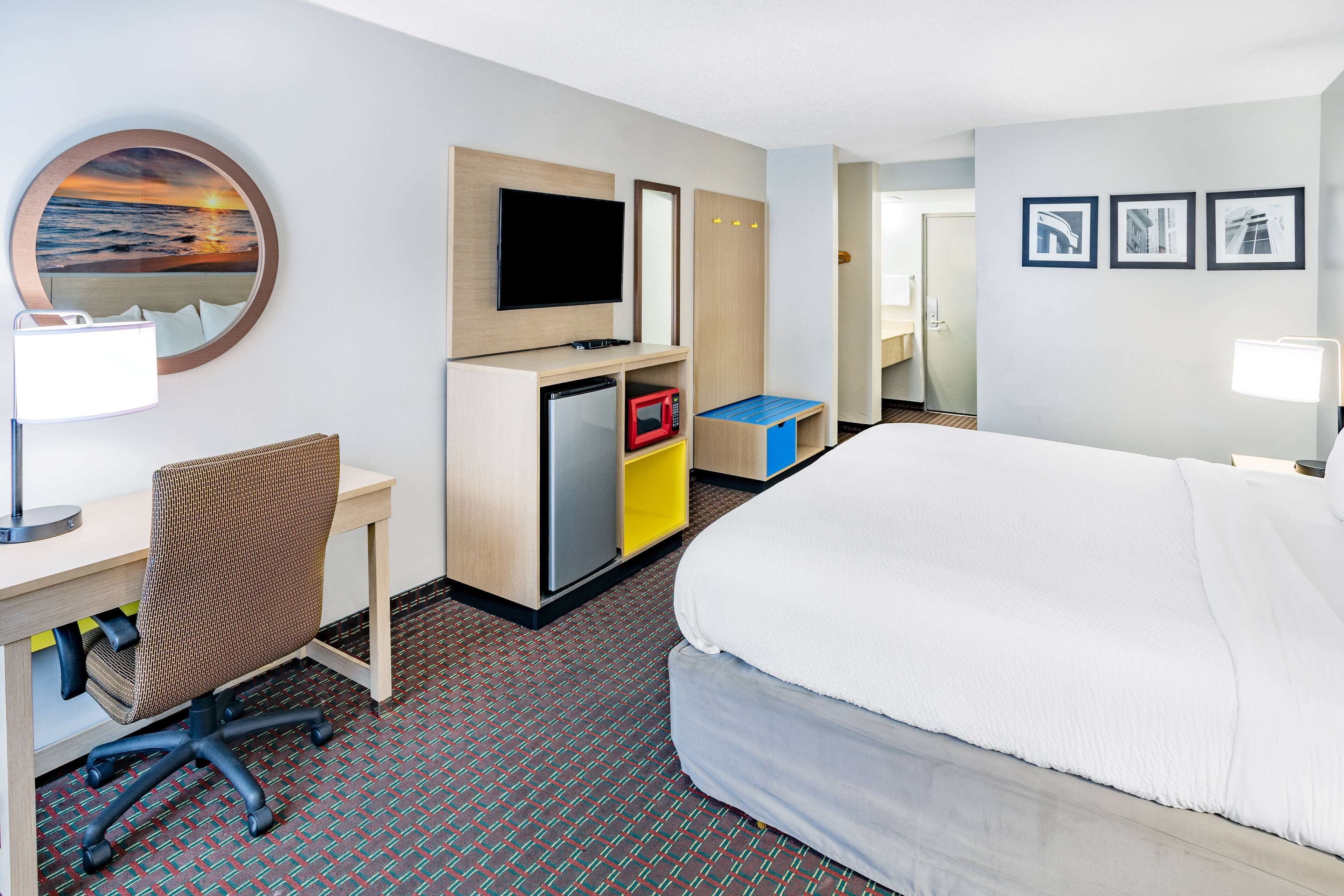 Habitación de hotel con cama, escritorio, silla, televisión y una pequeña kitchenette.