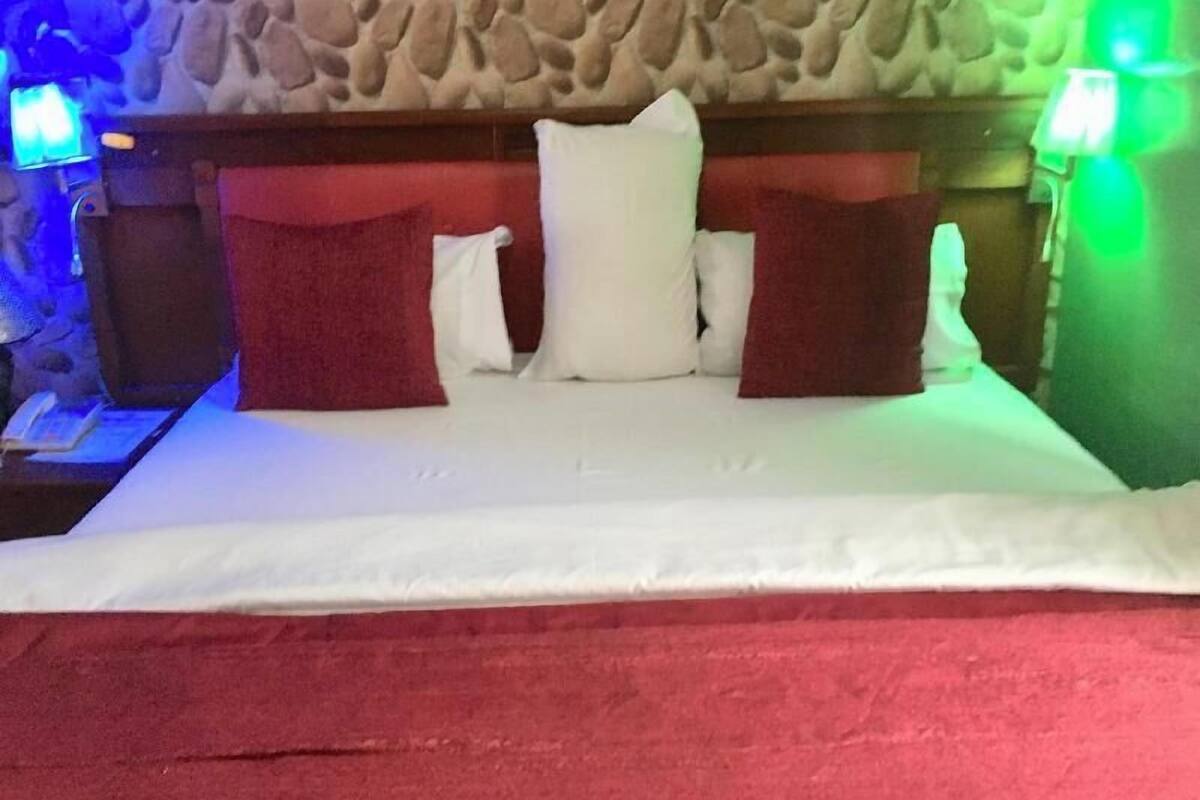 A hotel room with a stone wall, a bed with white bedding, red and white pillows, and two bedside lamps.