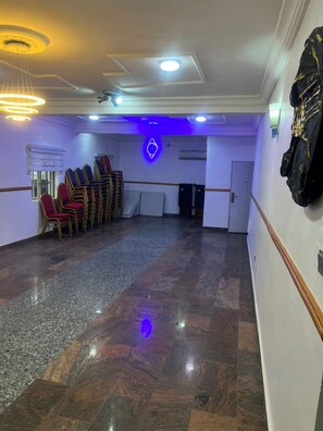 A room with a polished floor, stacked chairs, a neon sign, and a speaker system.