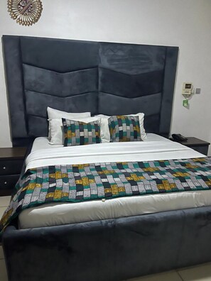 Un lit avec une tête de lit sombre, une literie blanche et un plaid à motifs.