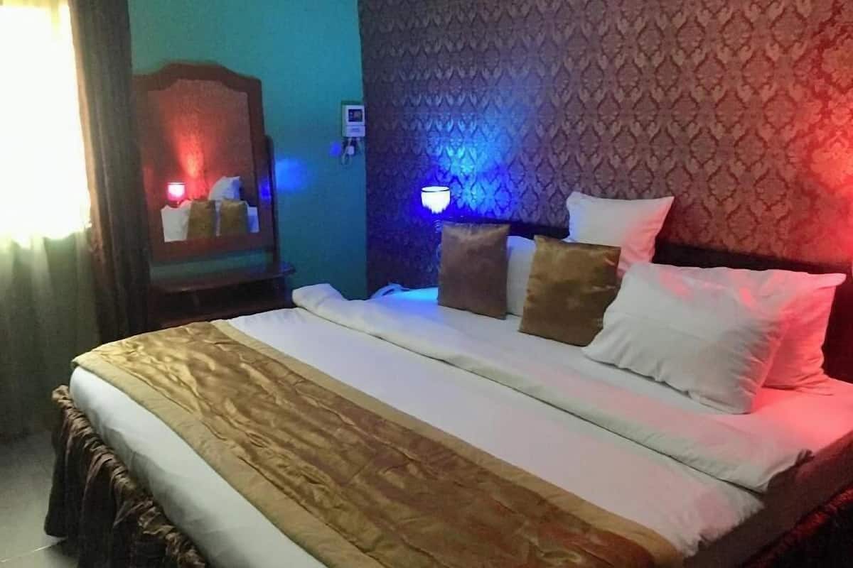 A hotel room with a bed, a nightstand, a mirror, and a wall-mounted light fixture.