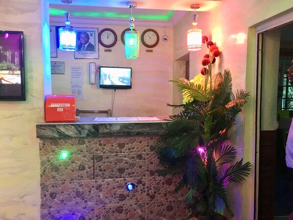 Un área de recepción con pared de piedra, un buzón de sugerencias, un reloj y un televisor.