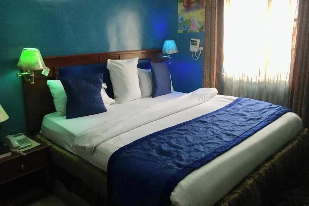 A hotel room with a bed, a nightstand, a lamp, and a window with curtains.