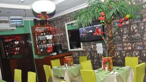 A restaurant interior with tables set for dining, a bar area with bottles, and a television screen on the wall. - Definite Destiny Hotel (Lagos)