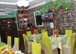 A restaurant interior with tables set for dining, a bar area with bottles, and a television screen on the wall. - Definite Destiny Hotel (Lagos)
