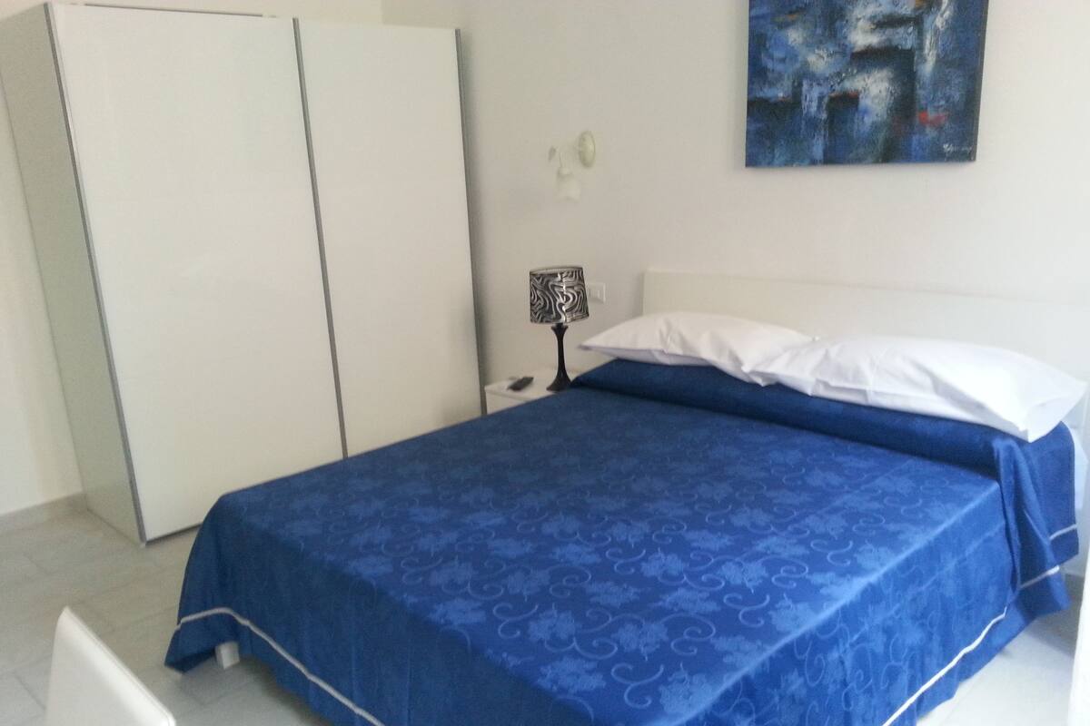 A bedroom with a bed, a wardrobe, a nightstand, and a painting on the wall.