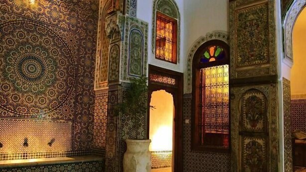 Interior tradicional com trabalhos em azulejos elaborados, uma porta grande e ornamentada e um vaso de planta.