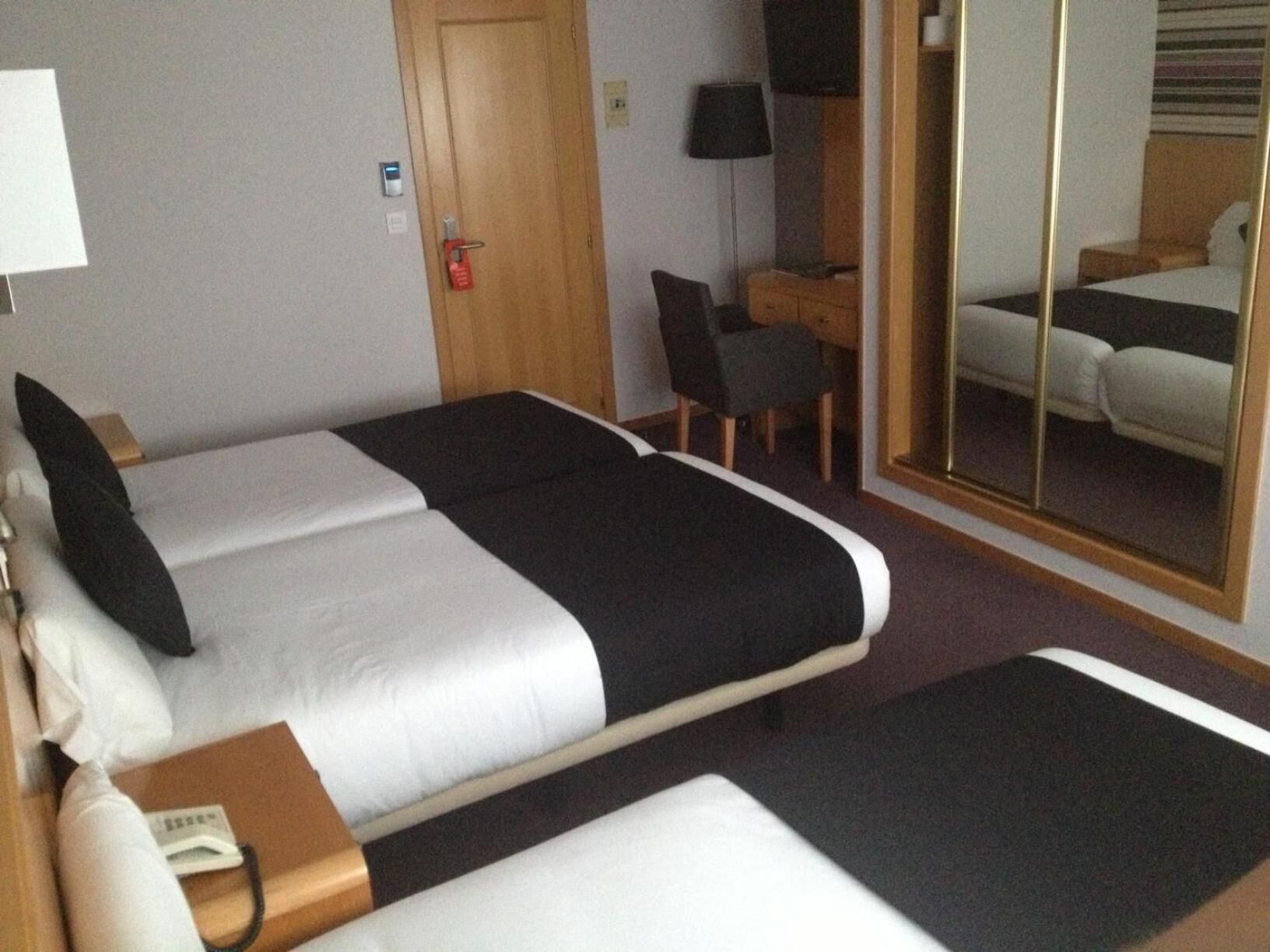 A hotel room with two beds, a desk, a chair, and a mirror.