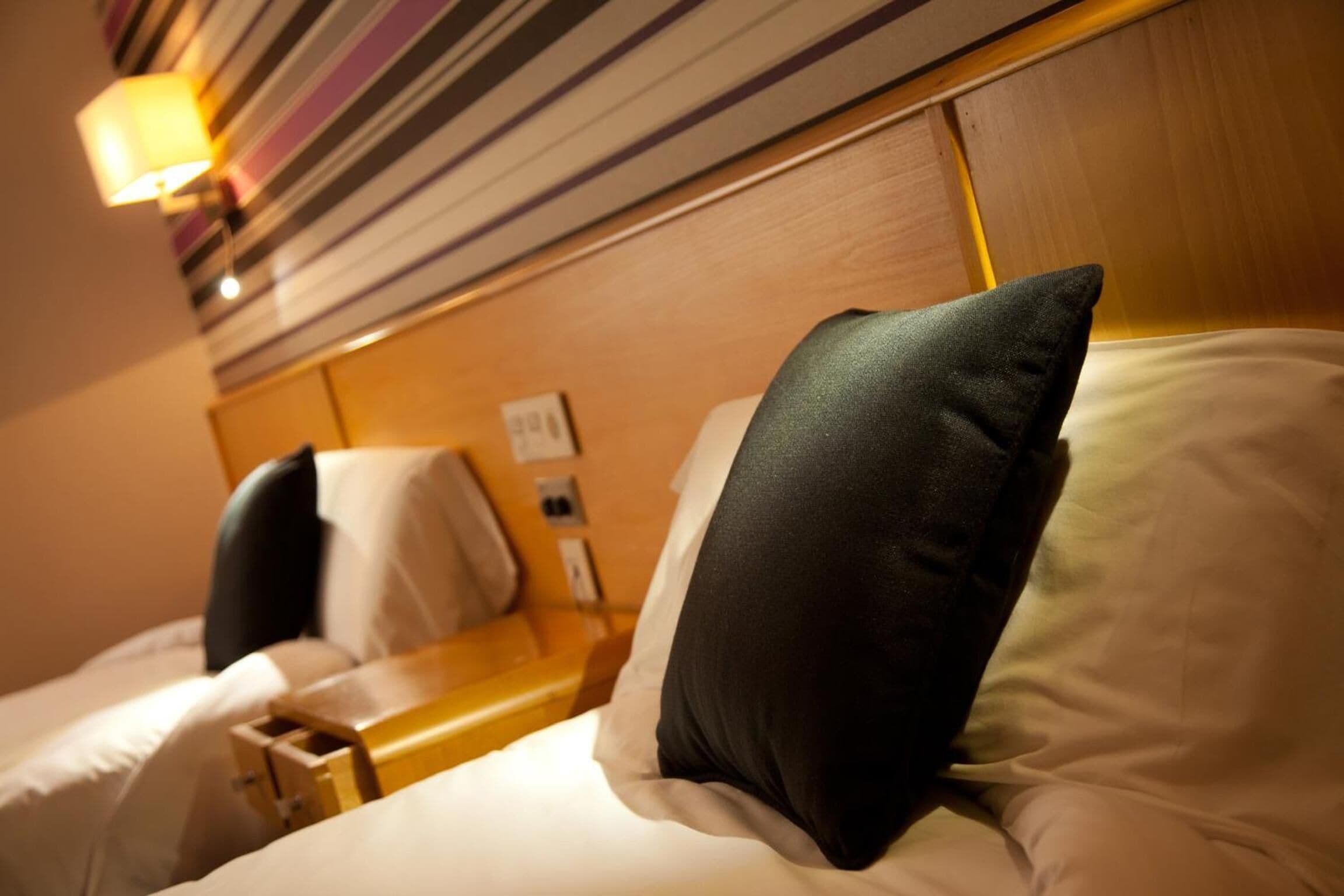 A hotel room with a wooden headboard, a bedside table, and a lamp.