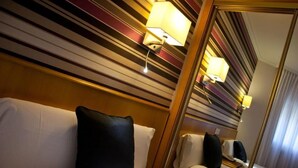 Habitación de hotel con techo a rayas, un espejo grande y una cama con sábanas blancas y almohada negra.