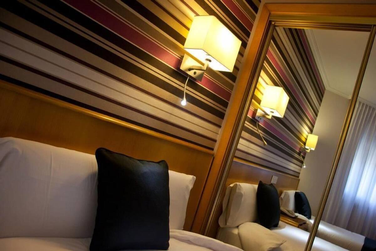 Habitación de hotel con techo a rayas, un espejo grande y una cama con sábanas blancas y almohada negra.