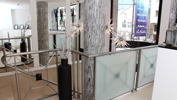 Un interior moderno con separador de vidrio, barandillas de metal y plantas decorativas.
