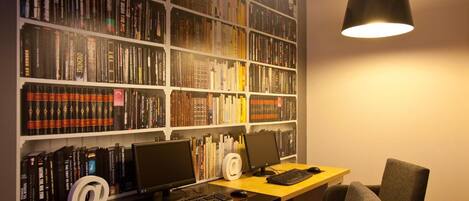 A home office with two desks, each with a computer and keyboard, and a large bookshelf filled with books.