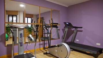 Ein Fitnessraum mit Laufband, Crosstrainer und Stepper, einem großen Spiegel und einer violetten Wand.