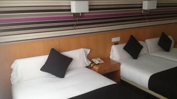 Habitación de hotel con dos camas, cada una con sábanas blancas y almohadas negras, cabecero de madera y mesita de noche con teléfono.