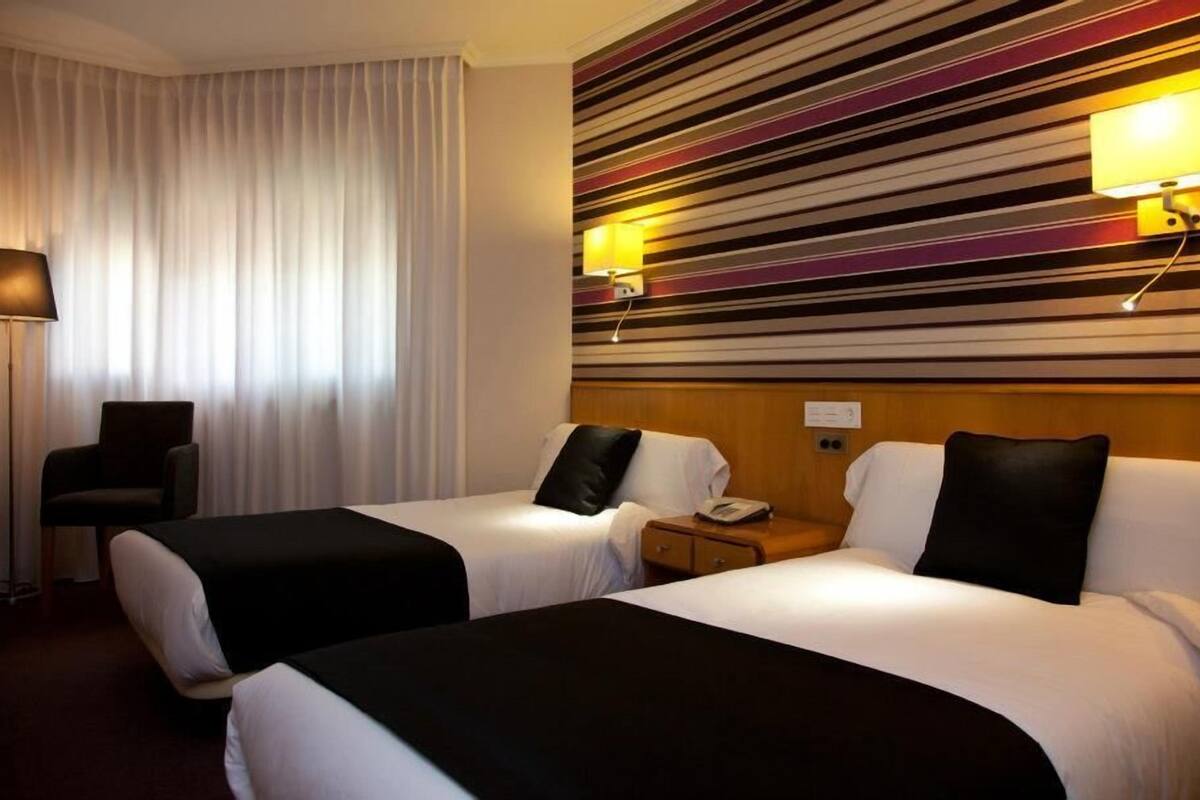 Habitación de hotel con dos camas, un escritorio, una silla, una lámpara y una pared a rayas.