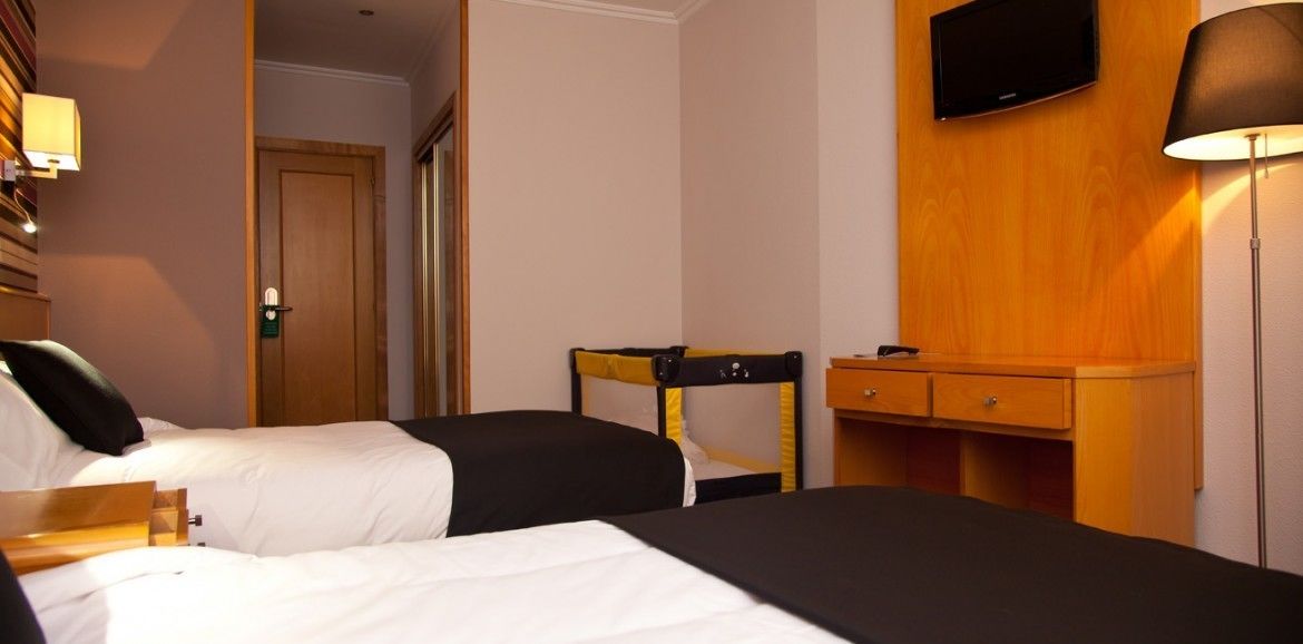 Habitació d'hotel amb dos llits, un escriptori de fusta, una televisió i una làmpada.