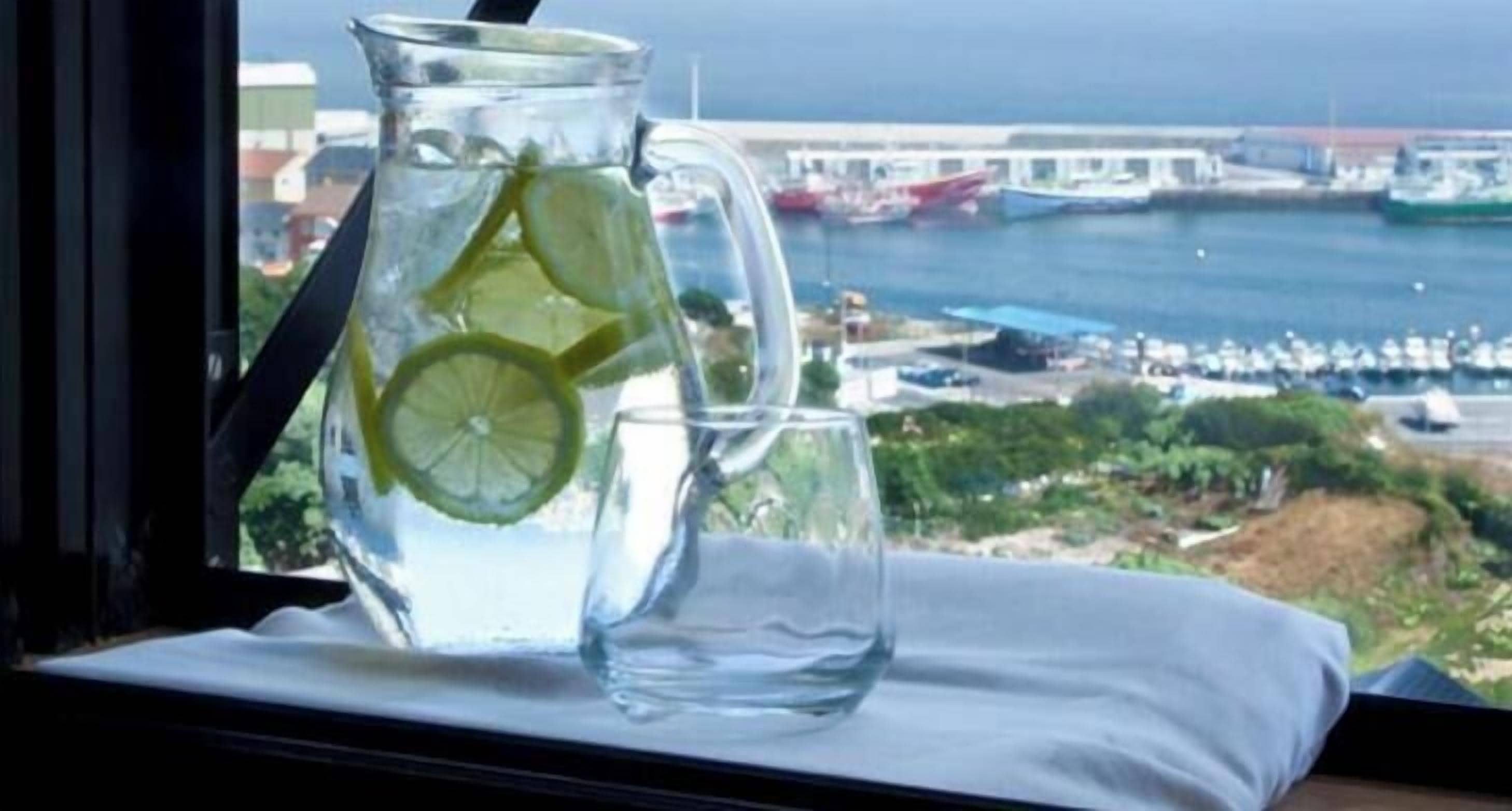 A pitcher and a glass of water on a windowsill with a view of a marina and boats.