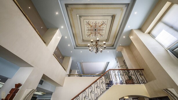 Ein mehrgeschossiges Interieur mit einer zentralen Treppe, einer verzierten Decke und eingelassener Beleuchtung.
