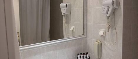 Une salle de bain avec un lavabo blanc, un miroir, un porte-serviettes et un sèche-cheveux fixé au mur.
