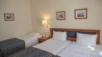 Een hotelkamer met twee eenpersoonsbedden, een tweepersoonsbed, een nachtkastje met een lamp, en twee ingelijste foto’s aan de muur.