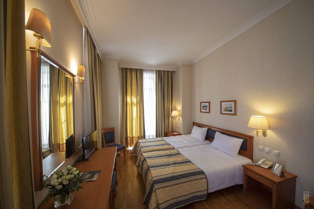 A hotel room with a large bed, two bedside tables, a desk, a chair, a mirror, and a window with curtains.
