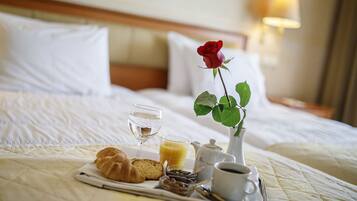 A neatly made breakfast tray on a bed with a red rose, a glass of juice, croissants, and a cup of coffee.