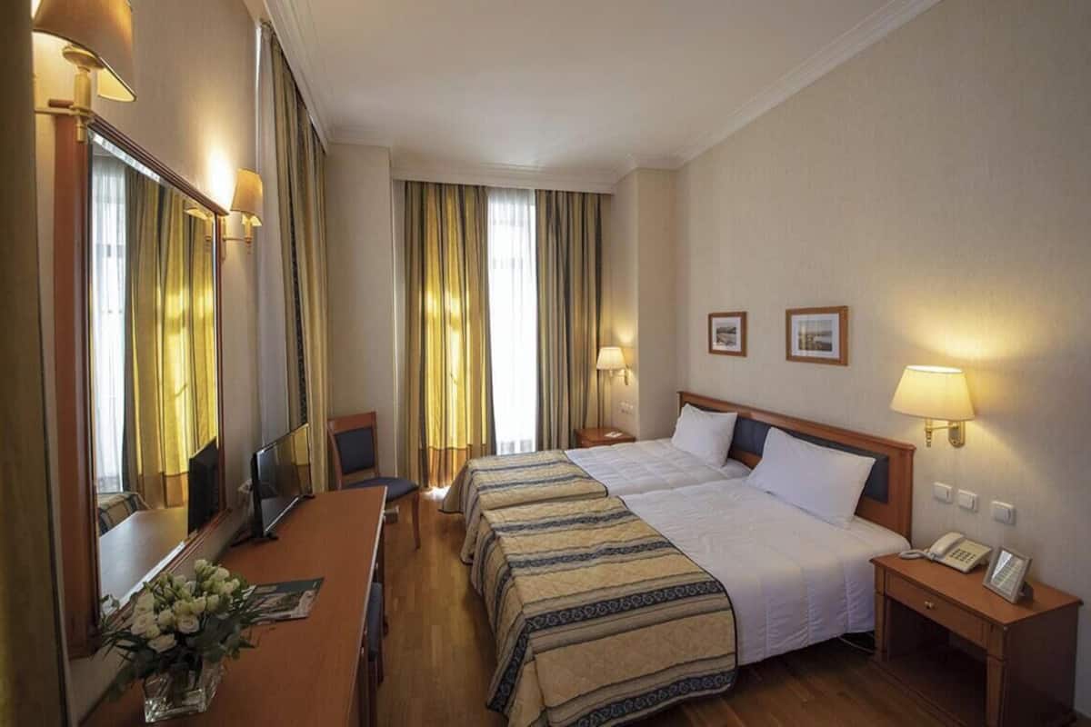 A hotel room with a bed, bedside tables, a desk, a chair, a mirror, and curtains.