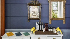 A white vanity with gold handles, two ornate mirrors, and a selection of toiletries on a tray. - Rex Hotel (Kalamata)